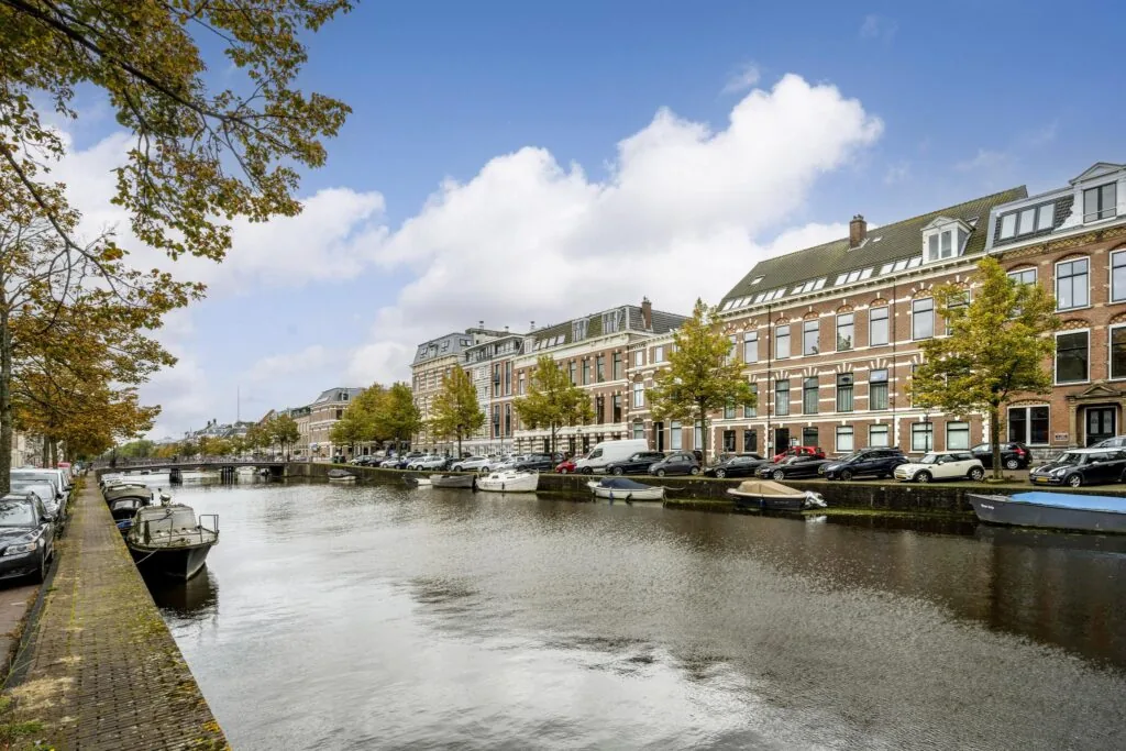 Herfstachtig straatbeeld aan de Nieuwe Gracht met grachtenpanden, geparkeerde auto's en boten in het water.